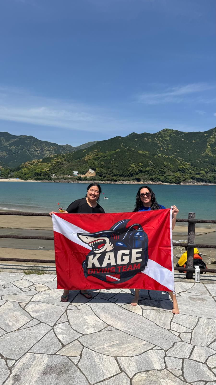 Luciana Babata Watanabe e colega segurando a bandeira da KAGE DIVING TEAM na praia de Atashika, Kumano, Mie